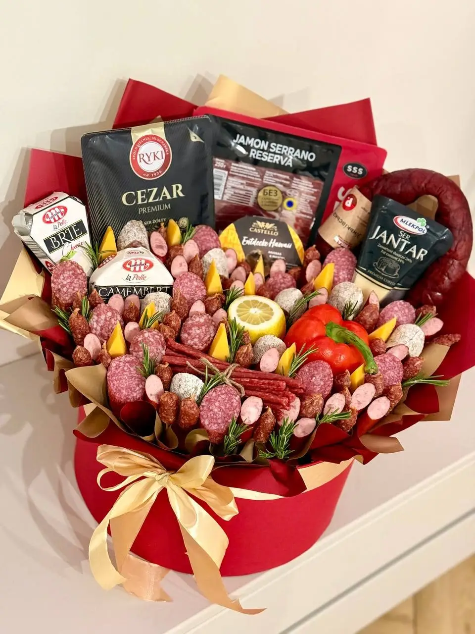 Гастрономічна композиція з ковбасками, сиром і овочами в червоній коробці
