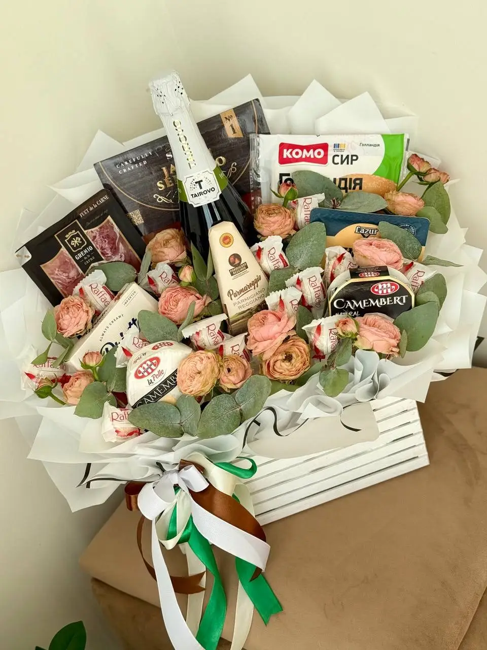 Композиція з ковбасками, сирами та ігристим у білій коробці з зеленню