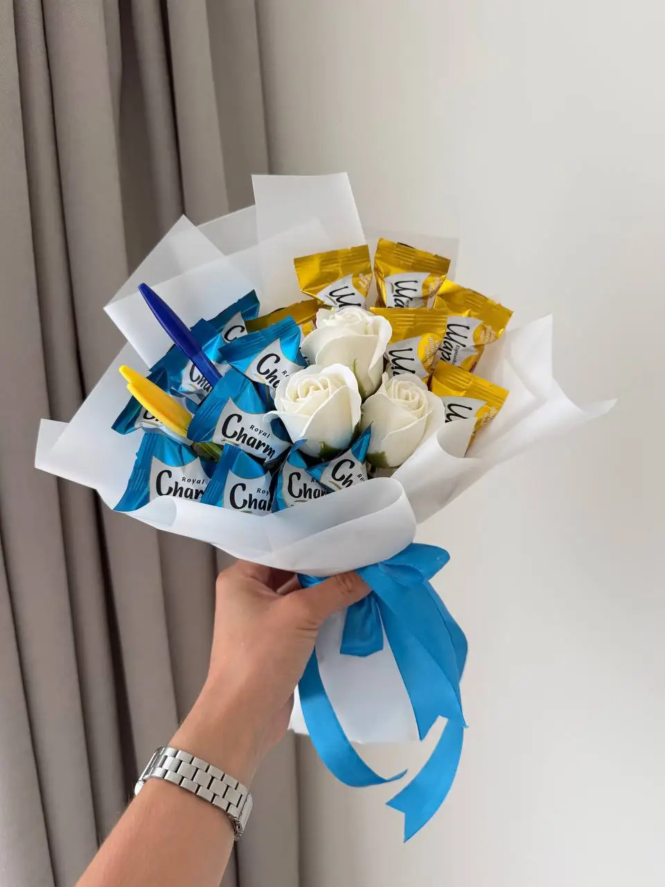 Букет із цукерок у синіх і золотих обгортках, білих мильних троянд та ручки, перев’язаний блакитною стрічкою